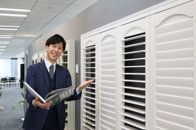 ウッドシャッターの前で笑顔で紹介している様子