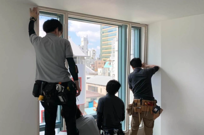 窓にウッドシャッターを取り付ける4人の男性スタッフ