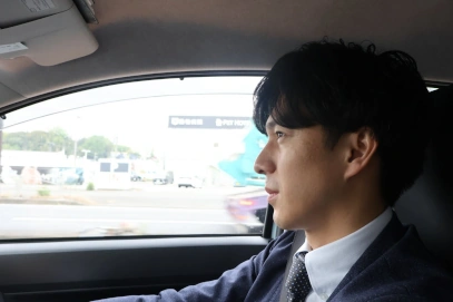 スーツとネクタイを着用した男性が車を運転している様子