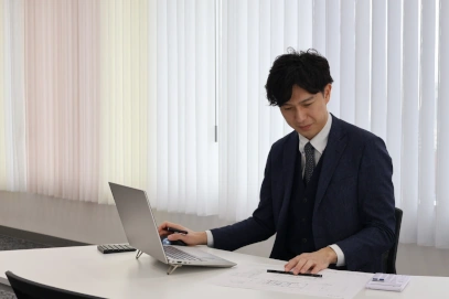 オフィスで図面を広げながら、ノートパソコンを前にデスクワークをするビジネスマン