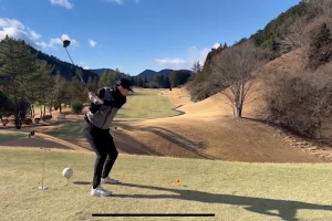 晴天のゴルフコースで、ドライバーショットを打つ男性。冬の景色が広がり、茶色い芝生と青い空が美しく調和している。