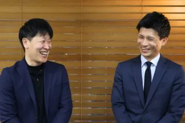 ノーマンジャパンの採用担当者2名（男性）がブラインドの前でほほ笑んでいる