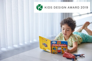 スマートドレープシェードの前で絵本を読む男の子とキッズデザイン賞マーク