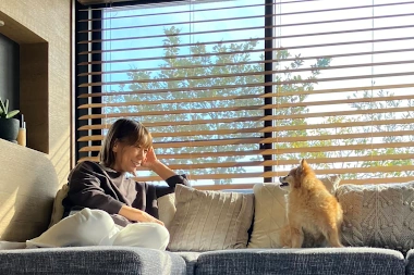 ウエスタンレッドシダーブラインドの前のソファで、くつろいでいる女性スタッフと愛犬のポメラニアン