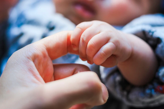 小さな赤ちゃんが、パパの指をやさしく握っている様子（イメージ画像）