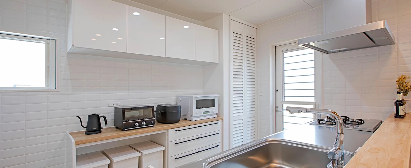 白いインテリアでまとめられたキッチン。パントリーの扉にウッドシャッターが取り入れられている